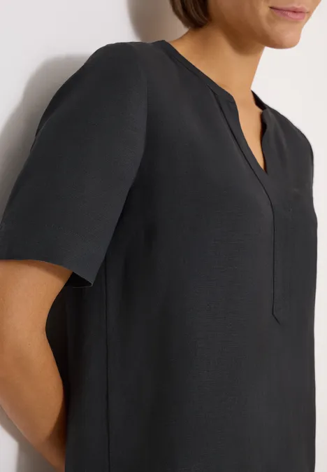 Close-up van een vrouw in zwart hemd met korte mouwen voor een witte achtergrond.