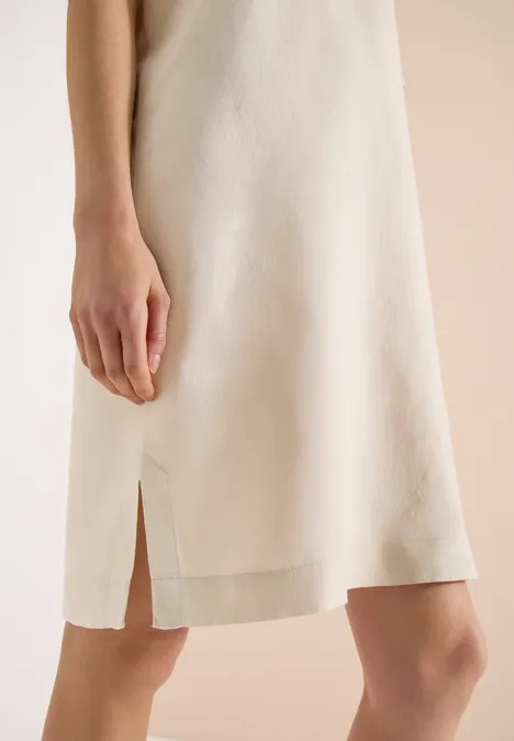Beige, knielange jurk met smalle bandjes en een split in de zijnaad.