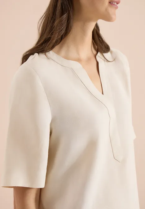 Vrouw in crèmekleurige blouse met V-hals en halflange mouwen