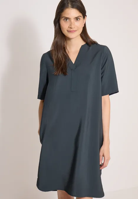 Knielanges Kleid mit Split Neck palm breeze green Eine Frau trägt ein locker geschnittenes, knielanges, dunkelgrünes Kurzarmkleid vor neutralem Hintergrund.