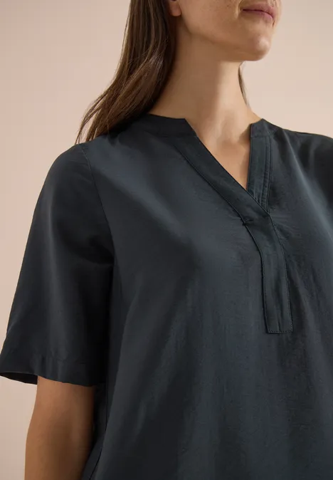 Knielanges Kleid mit Split Neck palm breeze green Eine Frau trägt ein dunkles Kurzarm-Oberteil mit V-Ausschnitt.