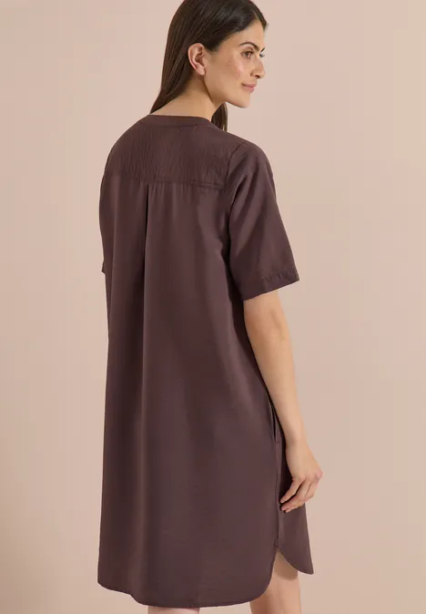 Vue de dos d'une femme portant une robe marron foncé, ample et mi-longue à manches courtes.
