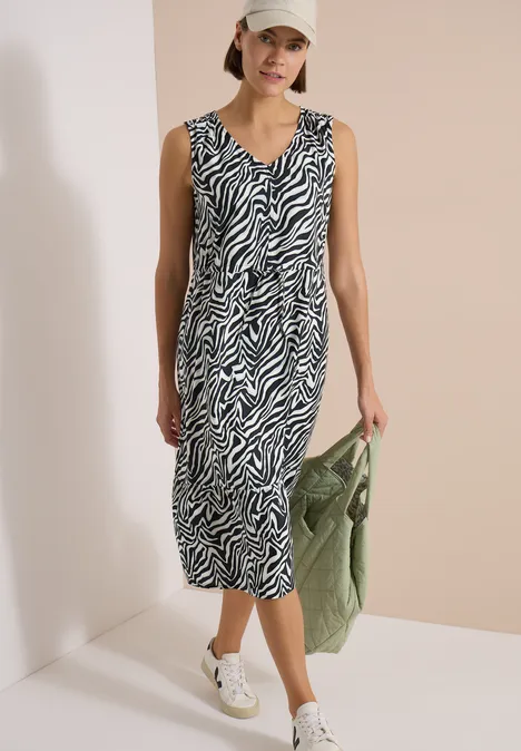 Vrouw in zebra-midi-jurk, witte sneakers en groene tas, casual en modern.