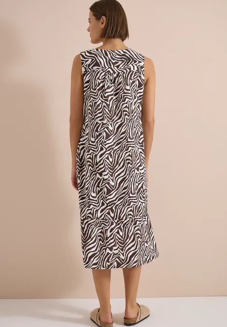 Vrouw van achteren in mouwloze midi-jurk met zebraprint, draagt platte sandalen.