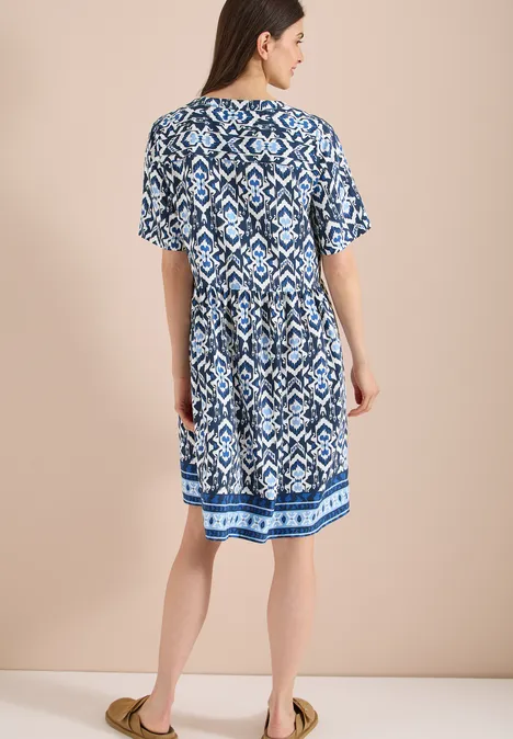 Rückenansicht eines blau-weiß gemusterten, kurzärmeligen Midikleids, kombiniert mit sandfarbenen Sandalen.