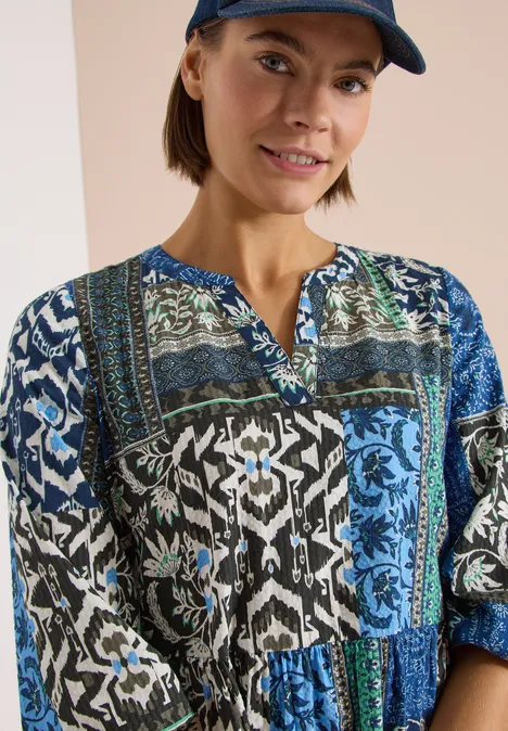 Femme portant une blouse patchwork aux motifs bleus, noirs et blancs à manches longues