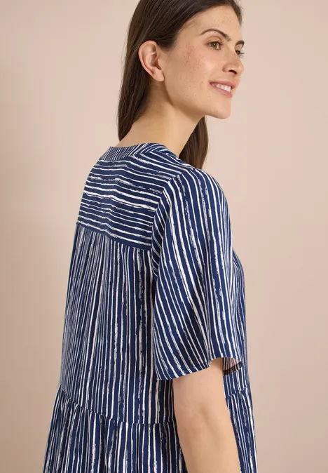 Eine Frau trägt seitlich fotografiert ein locker sitzendes blau-weiß gestreiftes Kleid.