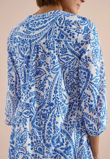 Vrouw van achteren in witte jurk met blauw paisleymotief en driekwart mouwen.