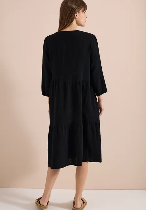 Frau von hinten in einem knielangen, schwarzen Stufenkleid mit 3/4-Ärmeln.