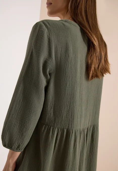 Frau von hinten in locker sitzendem, olivgrünem Kleid mit geraffter Taille.