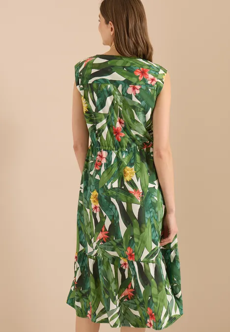 Vrouw van achteren in een groene mouwloze jurk met tropisch blad- en bloemenprint.