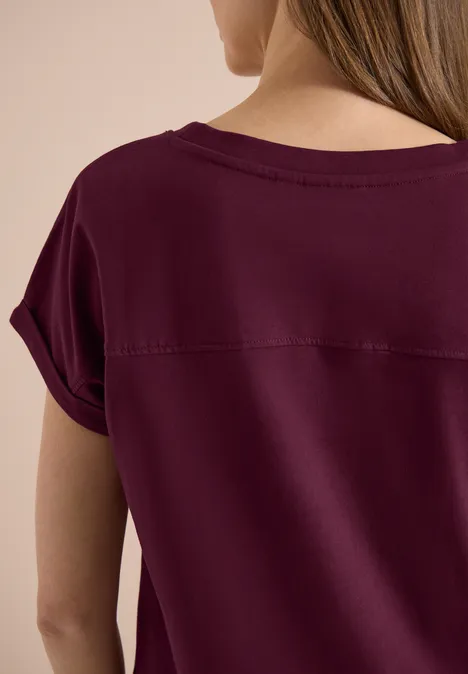 Vrouw van achteren in een bordeauxrood shirt met korte mouwen.