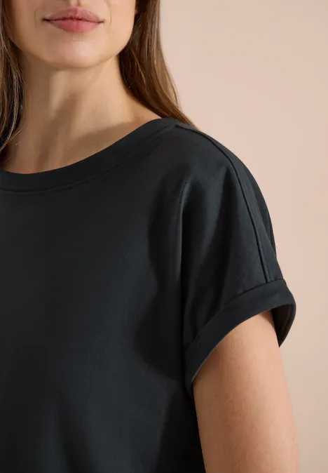 Close-up van een vrouwelijk bovenlijf in een eenvoudig zwart t-shirt met omgeslagen korte mouwen.