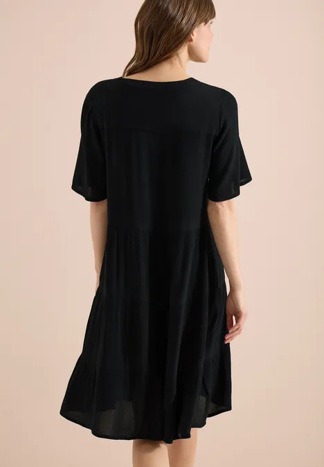 Vrouw in losvallende, zwarte jurk tot knie, korte mouwen, vloeiende stof, rugaanzicht