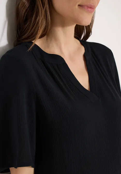 Effen zwarte damesblouse met V-hals en korte mouwen, subtiel geplooide stof bij het bovenlichaam.