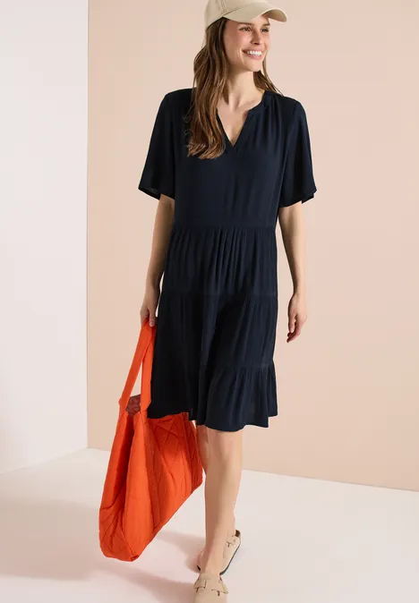 Frau in lockerem, schwarzem Kleid mit V-Ausschnitt trägt orangefarbene Tasche.