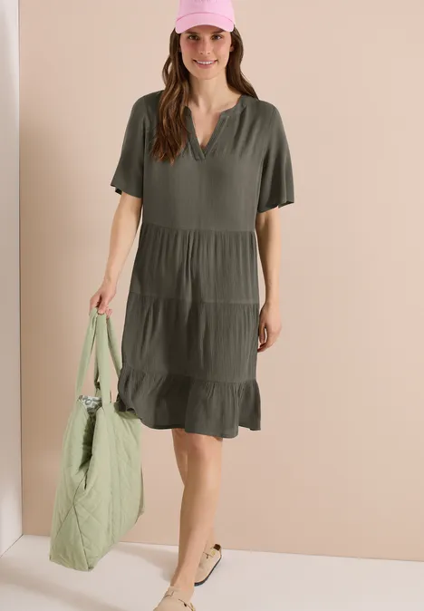 Vrouw in losvallende, olijfgroene jurk met volant, met een lichtgroene doorgestikte tas.
