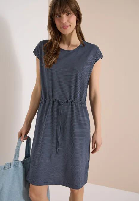 Vrouw in casual kort donkerblauw jurkje met taillekoord en korte mouwen, draagt een shopper