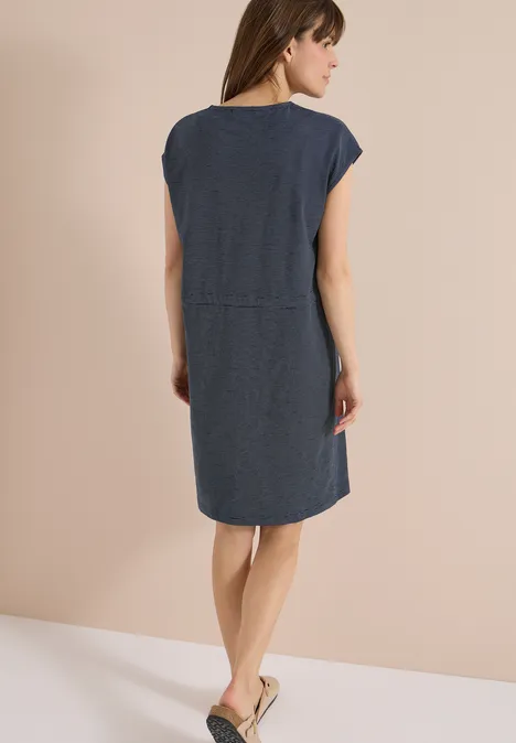 Achteraanzicht van een vrouw in korte spijkerjurk en platte sandalen.