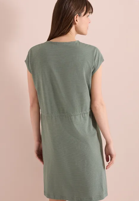 Vrouw met de rug naar de camera in een groen, kort mouw, knielang jurkje.