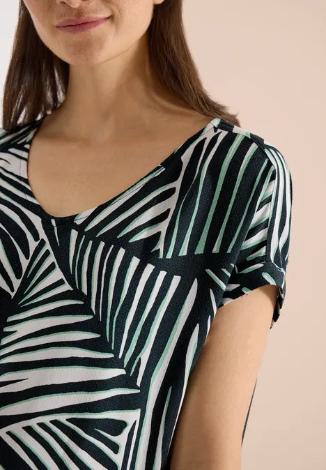 Vrouw in shirt met abstract patroon van zwart-wit-groene strepen.