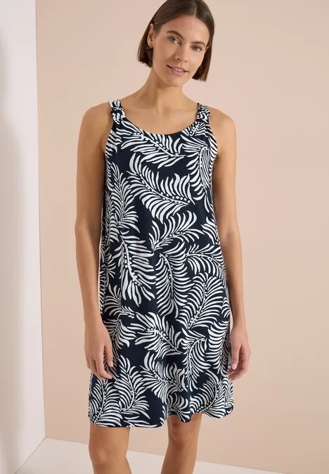 Vrouw draagt mouwloze knielange jurk marineblauw met wit bladmotief.