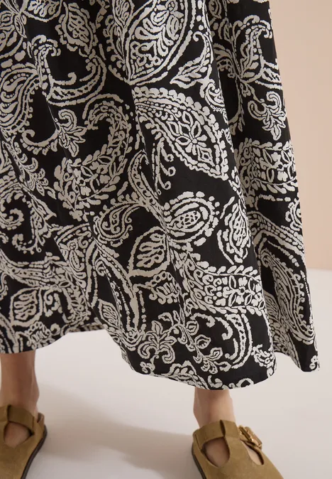 Schwarzer Maxirock mit weißem Paisley-Muster und braunen Sandalen.