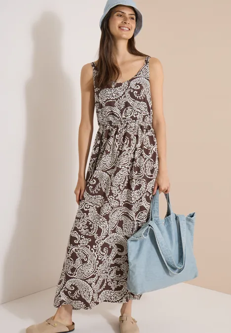 Maxikleid mit V-Neck und Print brown cacao Frau im ärmellosen Langkleid mit Paisley-Print in Erdtönen, dazu hellblauer Schultertasche.