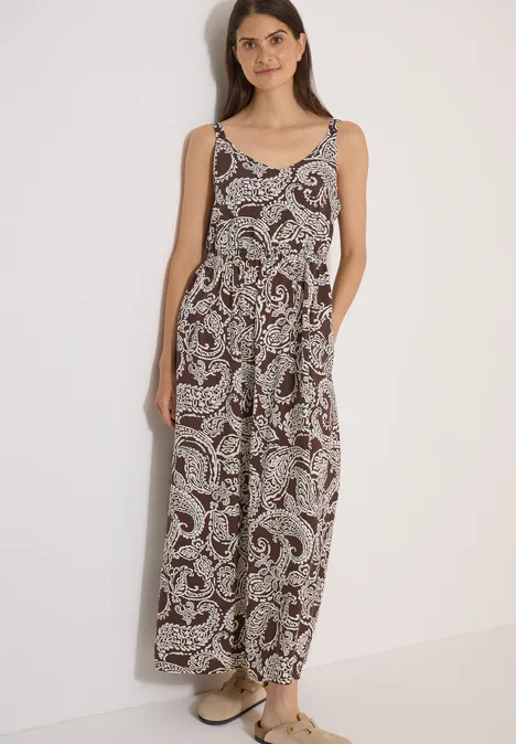 Maxikleid mit V-Neck und Print brown cacao Frau trägt ärmellosen, lockeren Jumpsuit mit Paisley-Muster und Sandalen vor hellem Hintergrund.