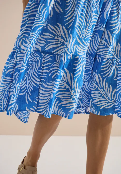 Frau in blau-weiß gemustertem, knielangem Kleid im Zebra-Design und Sandalen.
