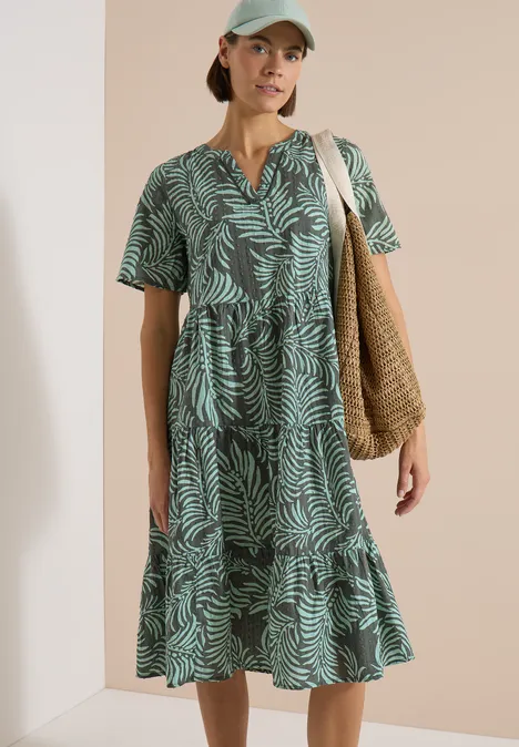Midikleid mit Split Neck und Print khaki Frau im grünen, kurzärmeligen Midikleid mit Blattmuster, V-Ausschnitt und Volant, trägt geflochtene Tasche.