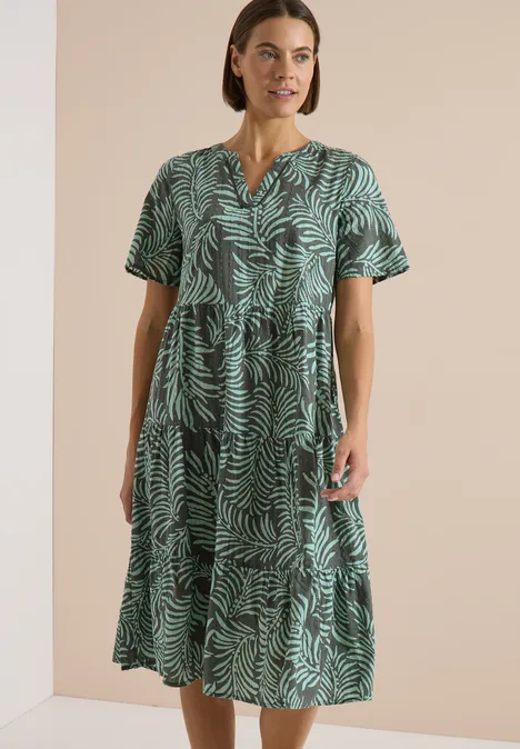 Midikleid mit Split Neck und Print khaki Frau trägt grünes, kurzärmeliges, wadenlanges Kleid mit Blattmuster und V-Ausschnitt.