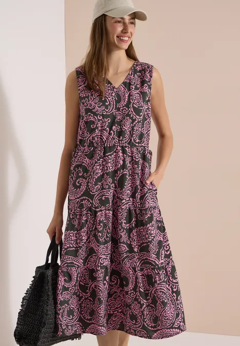 Midikleid mit V-Neck und Print raw khaki Frau in ärmellosem, lila gemustertem Midikleid mit Taschen, schwarzer Flecht-Tasche und beiger Kappe.