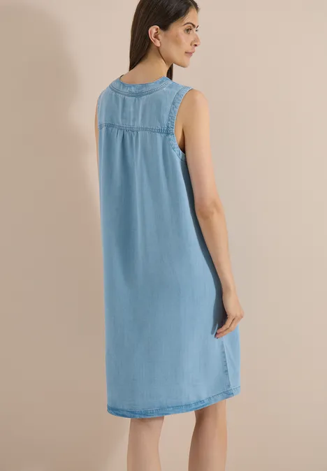 Frau in ärmellosem, knielangem, hellblauem Jeanskleid, Ansicht von hinten