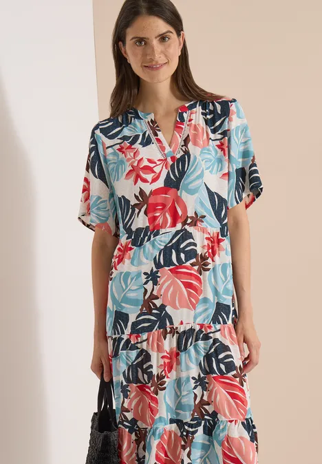 Vrouw in midi-jurk met kleurrijk tropisch bladprint.
