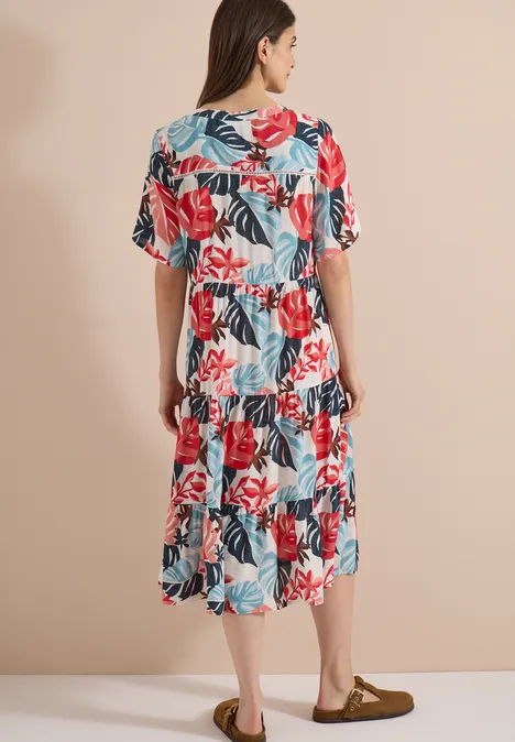 Achteraanzicht van een vrouw in een witte knielange jurk met bloemenprint en wijde mouwen voor neutrale achtergrond.