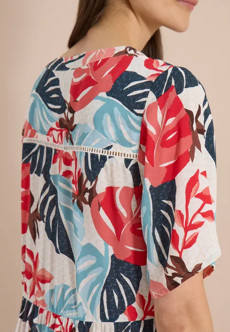 Vrouw van achteren in een wit shirt met rood-blauw tropisch bladerenpatroon en korte mouwen.