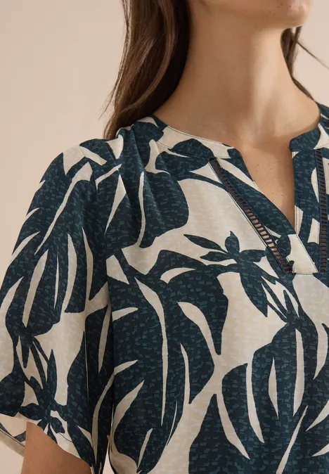 Robe mi-longue à col fendu et imprimé palm breeze green Femme portant un chemisier clair à motifs de feuilles tropicales foncées, col en V, mise au point sur le tissu.