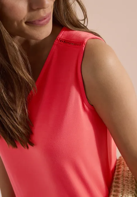 Knielanges Jerseykleid mit V-Neck coral Nahaufnahme einer Frau in einem roten, ärmellosen Top mit geflochtener Tasche im Hintergrund.