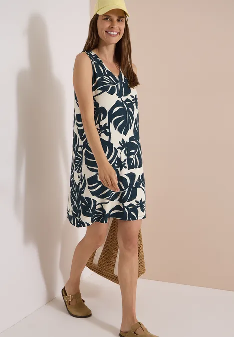 Knielanges Jerseykleid mit V-Neckund Print palm breeze green Frau im ärmellosen, knielangen Sommerkleid mit grünem Blattmuster, mit Basttasche und Slippern.