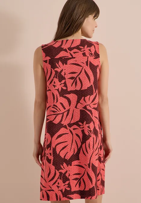Knielanges Jerseykleid mit V-Neckund Print coral Frau von hinten in ärmellosem roten Kleid mit großem rosa Blattmuster vor beigem Hintergrund.