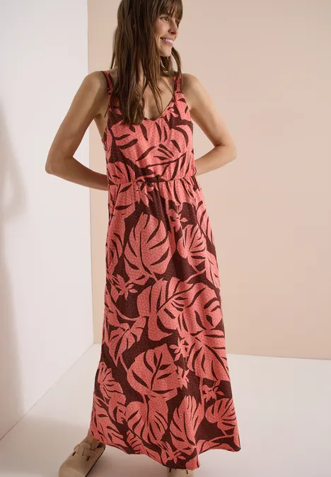 Maxikleid mit V-Neck und Print coral Frau in rotem Maxikleid mit pinkem Blättermuster, steht lächelnd mit Händen in der Hüfte.