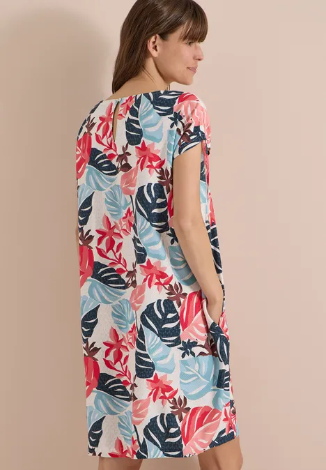 Robe mi-longue avec manchons light alabaster white Femme de dos portant une robe midi ample à manches courtes et motif de feuilles colorées.