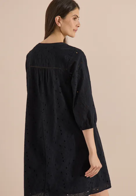 Vrouw van achteren in een zwarte tuniek met broderie anglaise en driekwartmouwen.