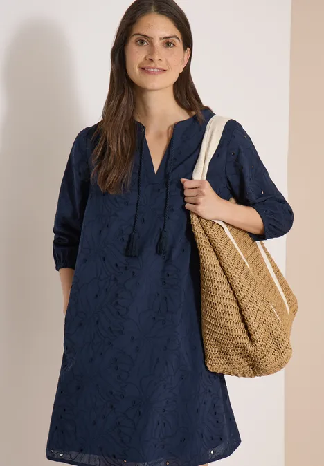 Robe longueur genou avec manches 3/4 et broderie universal blue Femme en robe bleu marine à broderie anglaise, manches mi-longues et sac en osier.