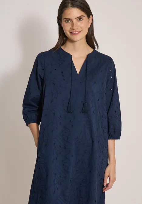Robe longueur genou avec manches 3/4 et broderie universal blue Une femme porte une robe bleu marine brodée, col en V, franges, manches 3/4 et poches.