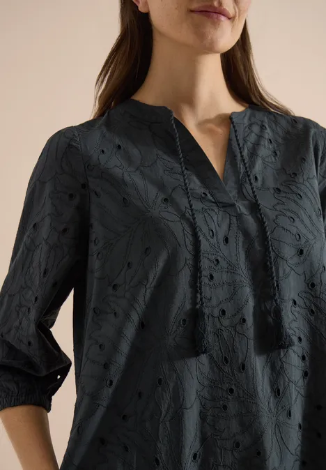 Een vrouw draagt een donkerblauwe blouse met bloemenknipwerk, driekwartmouwen en V-hals.