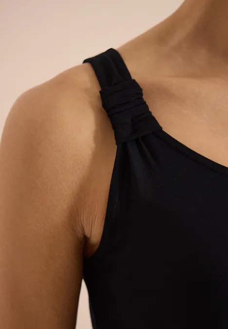 Close-up van een schouder met een zwart tanktopje met gedraaide band
