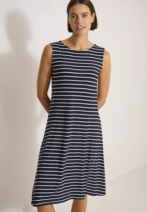 Femme en robe sans manches à rayures bleu et blanc sur fond neutre.