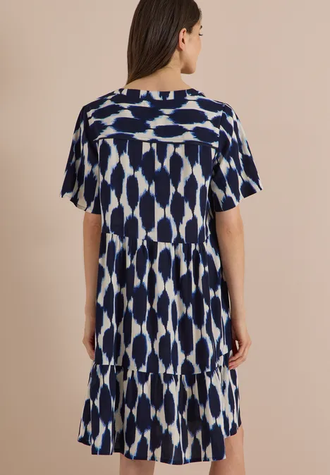 Knielanges Kleid mit Split Neck und Struktur urban dark blue Frau von hinten in einem kurzärmligen, blau-weißen, gemusterten Kleid mit Stufensaum.